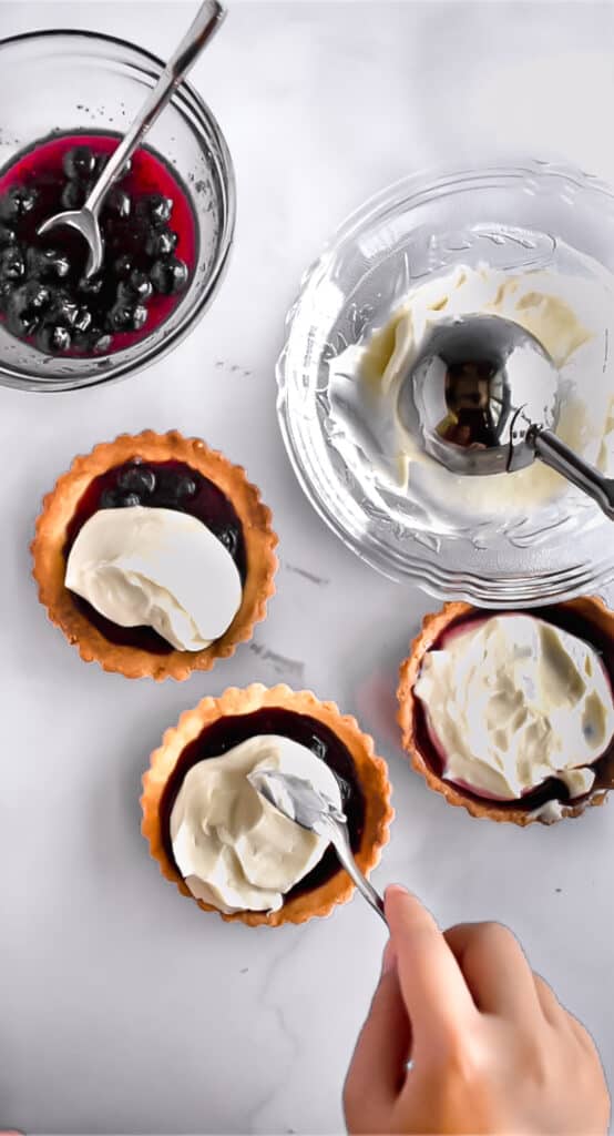 Cream cheese scooped on top of blueberry preserves in mini tart shells