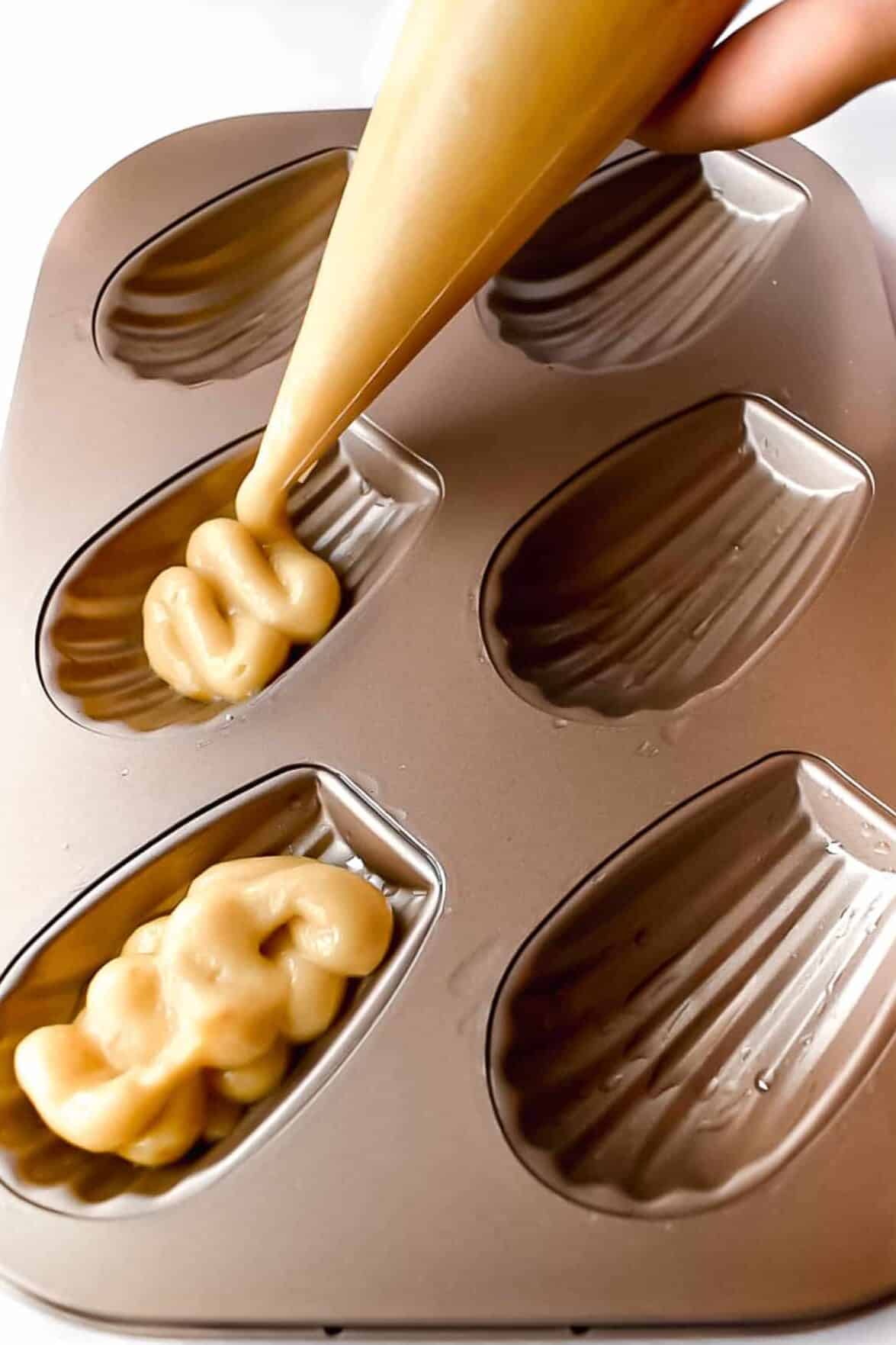Piping orange madeleine batter into sea shell shaped madeleine pan.