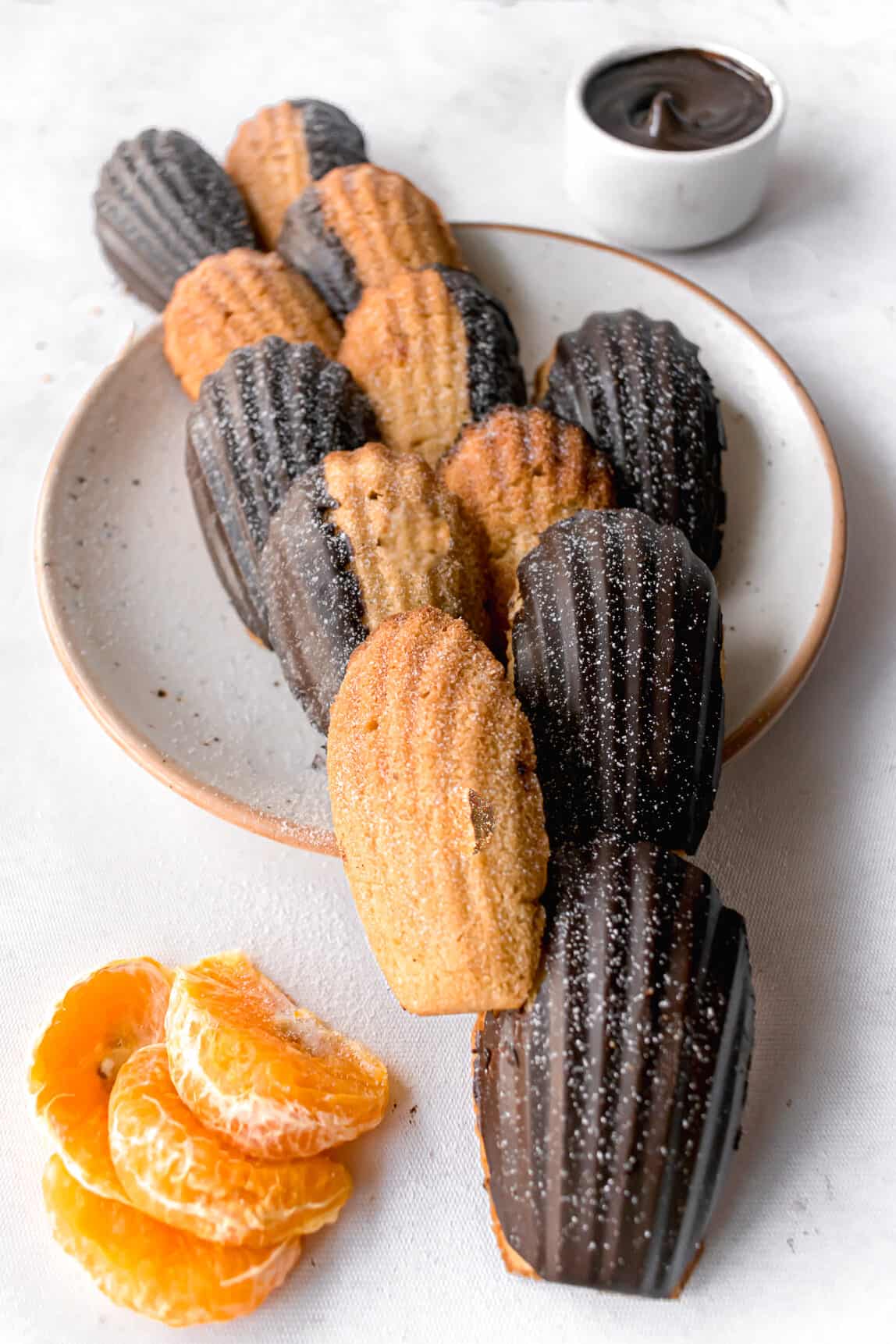 Chocolate glazed orange madeleines on a white plate with a brown rim.