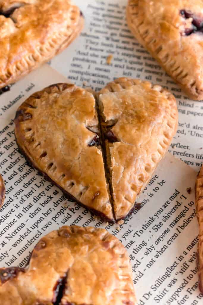 Heart shaped mini blueberry pies on a wooden board with one cut into two parts and divided into half