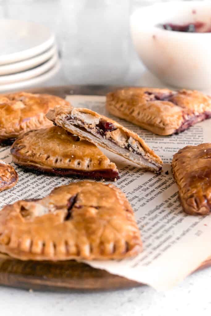 Heart shaped mini blueberry pies on a wooden board with one cut into two parts with flaky layers of pie crust